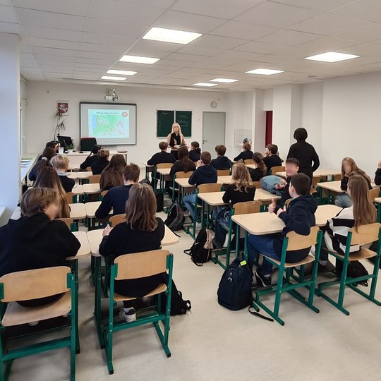 Septintokai stebi prezentaciją apie piliakalnių radinius, sėdėdami savo klasės suoluose.