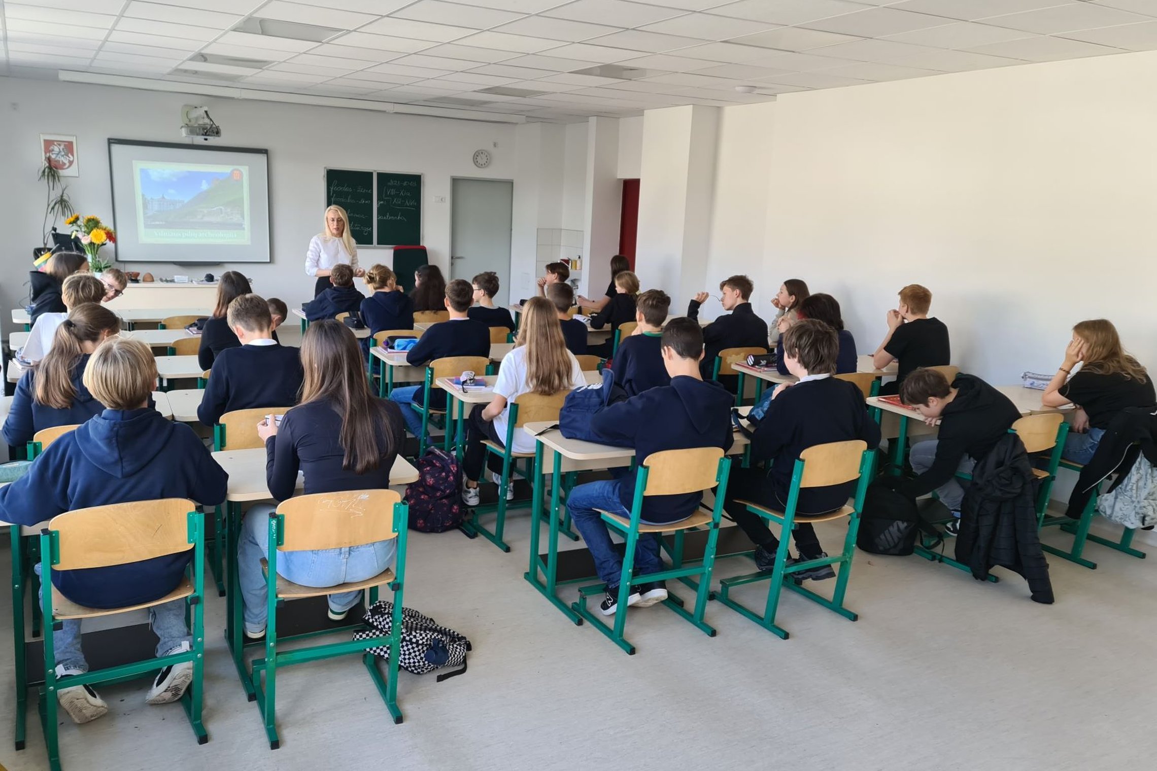 Šviesioje, baltoje, pilkomis sienomis, tačiau užpildytoje mokiniais klasėje vyko archeologijos paskaita. Septintokai klausėsi dėstytojos pasakojimų ir stebėjo projektoriaus rodomą ekraną.