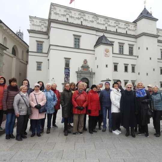 Nuotraukoje galima matyti grupę pagyvenusių žmonių, kurie stovi Katedros aikštėje. Galima pasakyti, kad jie yra ekskursijoje, nes vienas vyras, stovintis nuotraukos dešinėje pusėje, laiko fotoaparatą.