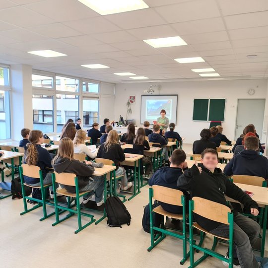 Nuotraukoje pavaizduota septintokų klasė, klausanti mokytojos pasakojimo. Paskutiniame suole, iš dešinės, arčiausiai kameros, vaikinas rodo liuksą, rodydamas, jog pamoka tikrai įdomi. Mokiniai įdėmiai stebi ir klauso mokytojos pasakojimo apie Vilniaus pil