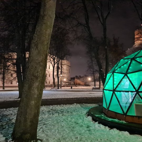 Vilniaus pilių kupolas iš lauko vakare. Tolumoje matosi Valdovų rūmų muziejus, dešinėje viršuje Gedimino kalnas su bokštu. Pats Vilniaus pilių kupolas šviečia žaliai.