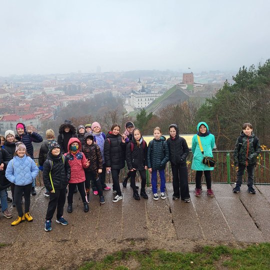 Mokiniai pozuoja nuotraukai ant Trijų Kryžių kalvos. Už nugaros matosi Gedimino kalnas ir Vilniaus panorama.