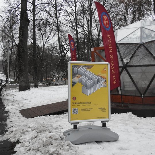 Vilniaus pilių kupolas su vėliavomis iš lauko pusės. Šalia kupolo afiša su geologo daktaro Jono Satkūno paskaitos informacija.