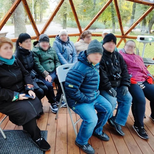Nuotrauka vaizduoja grupelę žmonių susėdusius stiklinio kupolo viduje. Šioje grupelėje yra ir suaugusių, ir vaikų, kurie visi žiūri tiesiai į kamerą. Jie yra apsirengę su striukėmis arba paltais. Aplinkoje matosi parkas su daug medžių, takeliais ir keliai