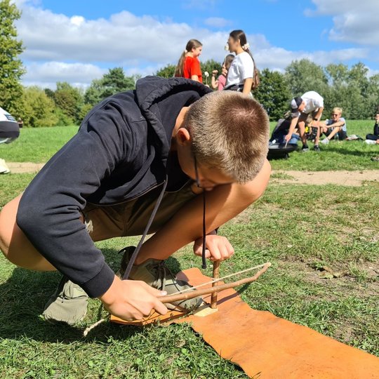 Vienas iš mokinių išbando, kaip kurti ugnį naudojantis pagaliuku ir lentele.