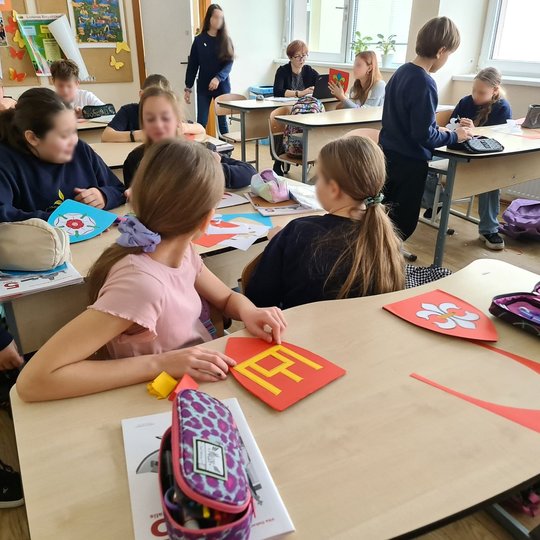 Mergaitė klasės suole laiko rankose raudoną herbą su Gediminaičių stulpais.