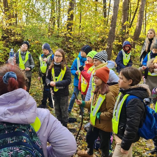 Edukatorius Vytas pasakoja apie Olandų gatvės pavadinimą ant Bevardžio piliakalnio. Aplink sustoję mokiniai klausosi.