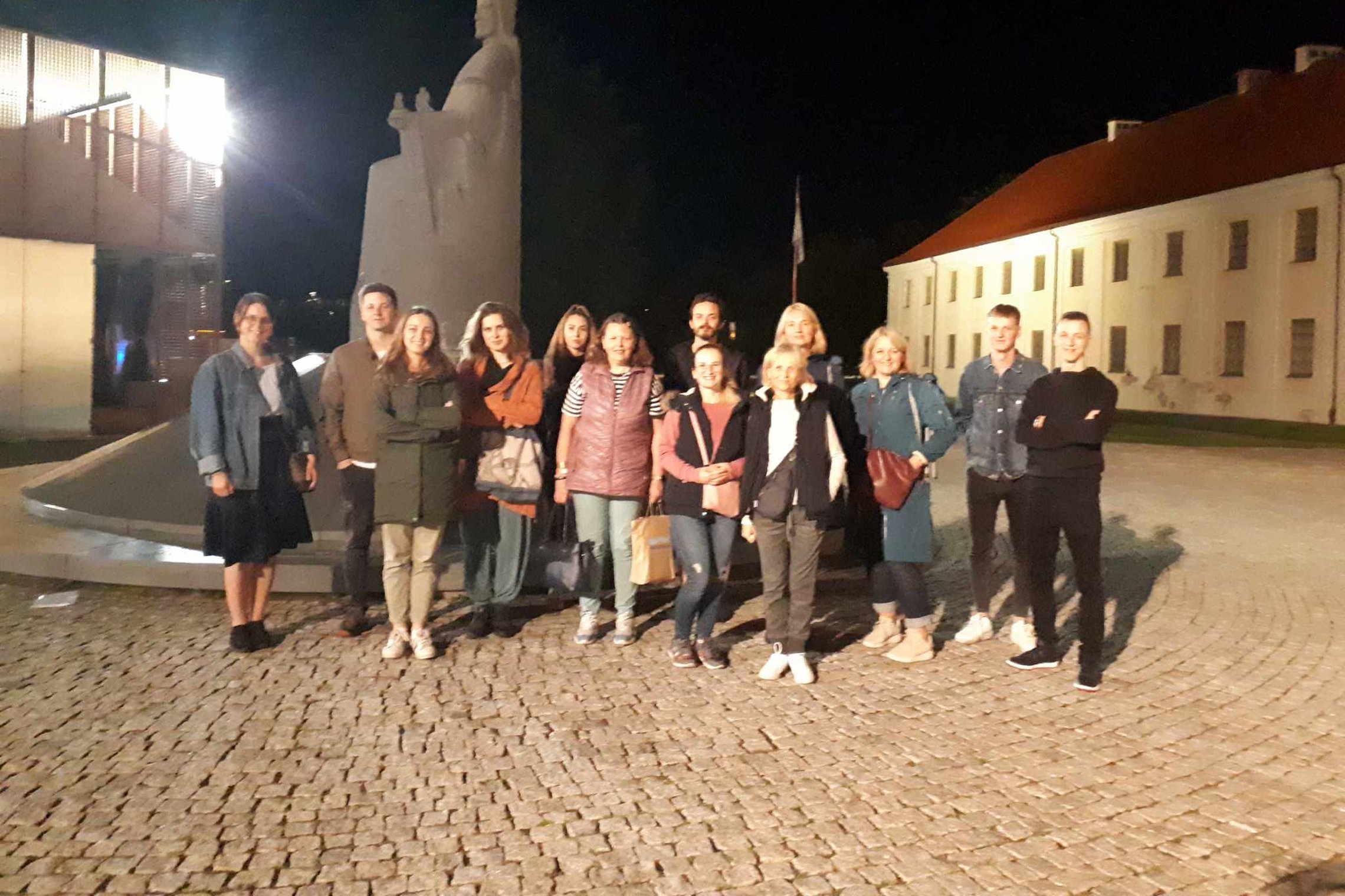 Trylikos dalyvių ekskursantai, sustoję prie Karaliaus Mindaugo paminklo.