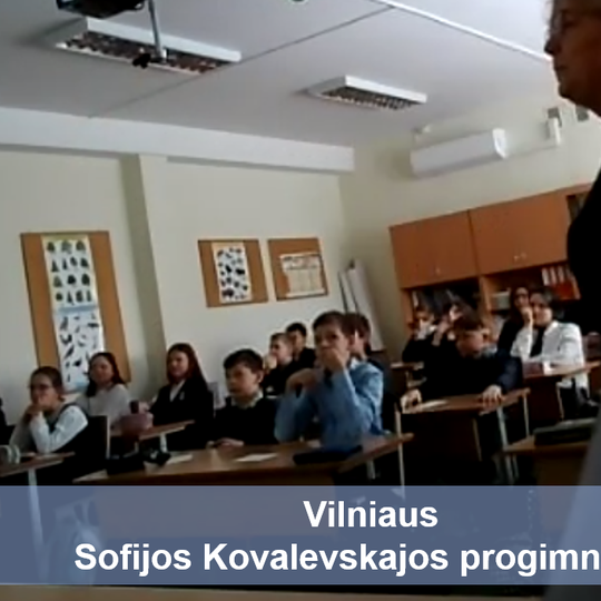 Mokiniai sėdintis klasėje. Priešais nuotrauką užrašas mėlyname fone "Vilniaus Sofijos Kovalevskajos progimnazija".