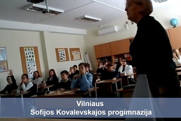 Mokiniai sėdintis klasėje. Priešais nuotrauką užrašas mėlyname fone "Vilniaus Sofijos Kovalevskajos progimnazija".