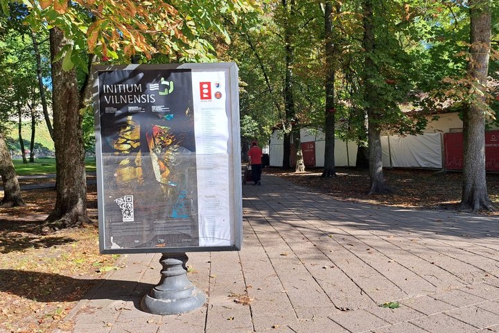 Nuotraukoje stovi reklamos skydas. Jame reklamuojama paroda Initium Vilnensis - žemės ir aplinkos menas, kuris buvo eksponuojamas Vilniaus pilių teritorijoje. 