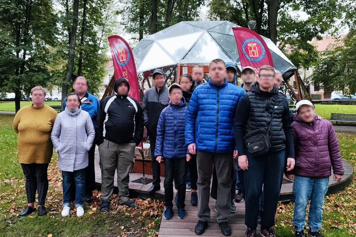 Grupelė įvairaus amžiaus žmonių yra sustoję nusifotografuoti, tiesiai už jų matosi Vilniaus pilių kupolas. 