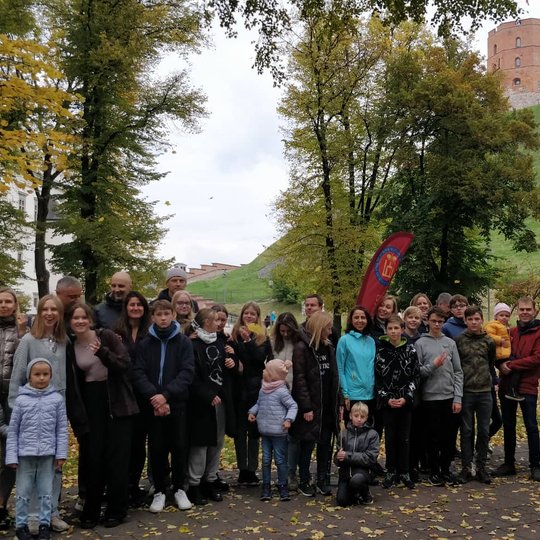 Vilniaus jėzuitų gimnazijos septintokais ir jų tėveliais Pilių parke pozuoja bendrai nuotraukai. Dešinėje viršuje Gedimino pilies bokštas.