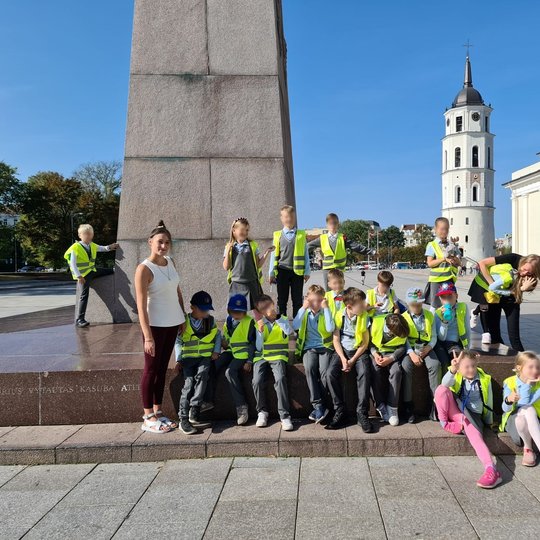 Vaikai stovi ant mažo takelio ir laikydami rankose titnagą ir metalinį gabaliuką bando įžiebti kibirkštį.