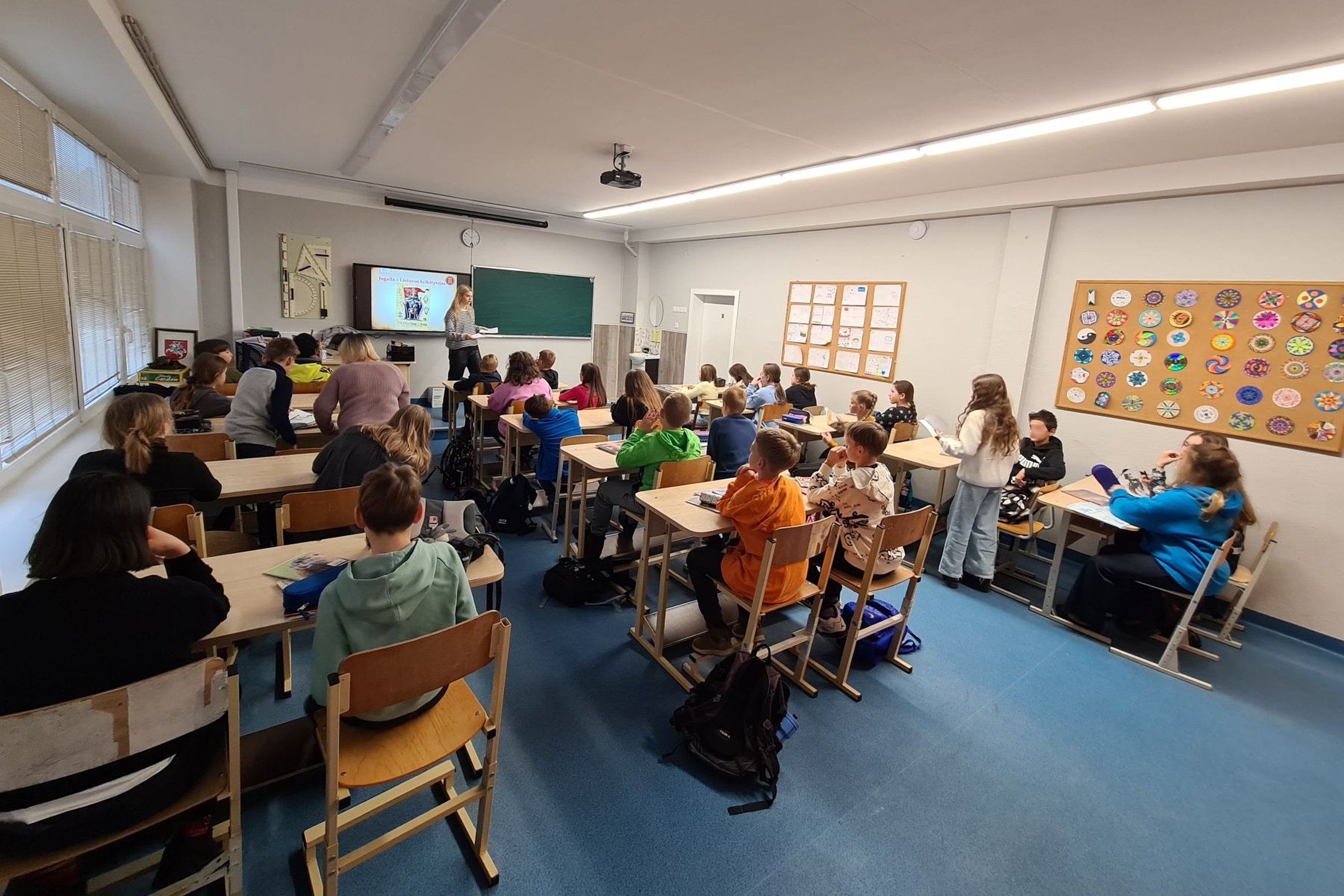Penktokai sėdi klasės suoluose. Fotografuoti iš klasės galo.