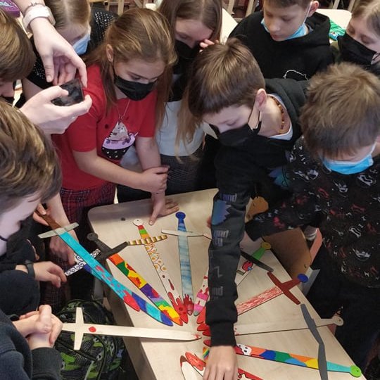 Vaikai su mediniais kalavijai klasėje. Mediniai kalavijai apskritimu sudėti į centrą.