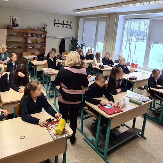 Vaikai ruošiasi istorijos pamokai klasėje. Tarp jų vaikšto ir mokytoja.