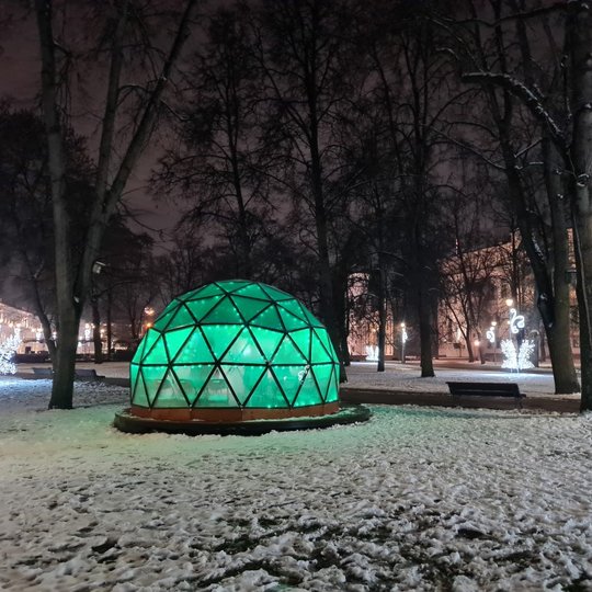 Žaliai šviečiantis Vilniaus pilių kupolas žiemos vakarą. Aplink baltas sniegas, tolumoje dešinėje matosi Valdovų rūmų muziejus.