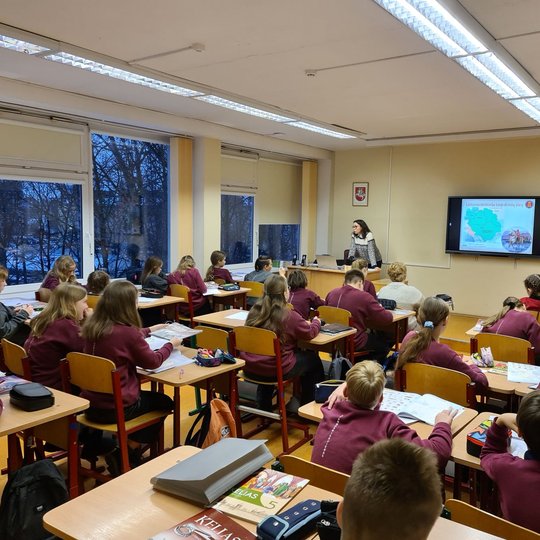 Klasėje, pilnoje mokinių, edukatorė veda istorijos pamoką.