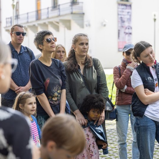 Įdėmiai besiklausantys gidės pasakojimo ekskursijos dalyviai.