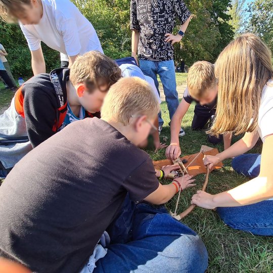 Nuotraukoje galima pamatyti mokinius ant Stalo kalno. Keturi iš jų yra susėdę į ratą ir jo viduryje turi pasidėję lanką. Vaikai aiškinasi, kaip juo naudotis.