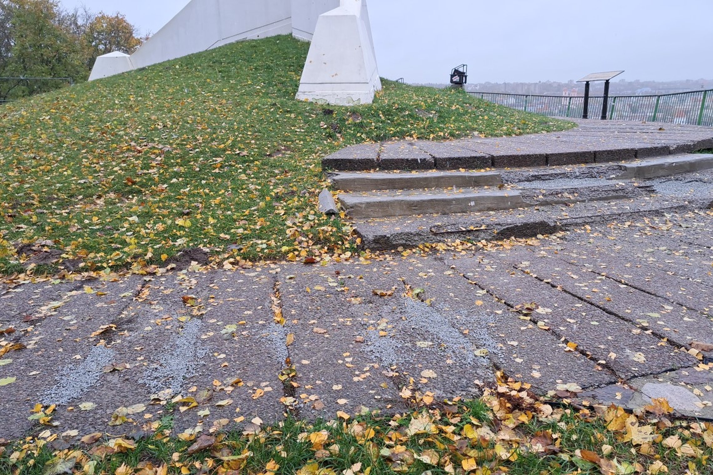 Nuotraukoje matosi Trijų kryžių kalno aikštelės laiptai. Jie nutrupėję, o jų ertmės užpiltos skalda. Ant nedidelio, žole apaugusio kalniuko, stovi Trys Kryžiai. Už žalių turėklų matosi Vilniaus senamiestis.