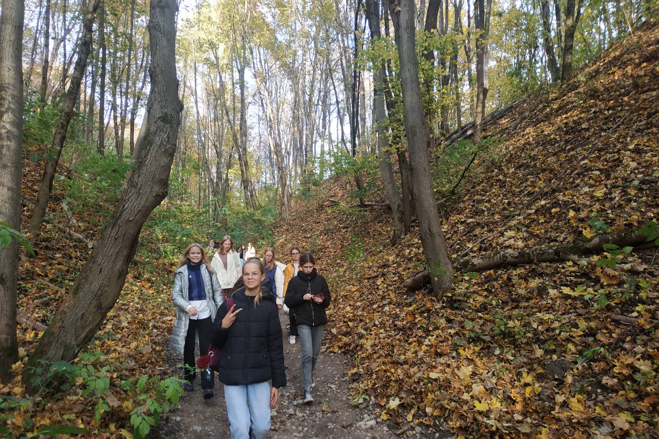 Šviesus rudens vakaras. Mergaitės leidžiasi žemyn Didžiąja Griova. Šlaituose matosi medžiai ir ant žemės nukritę gelsvi lapai.