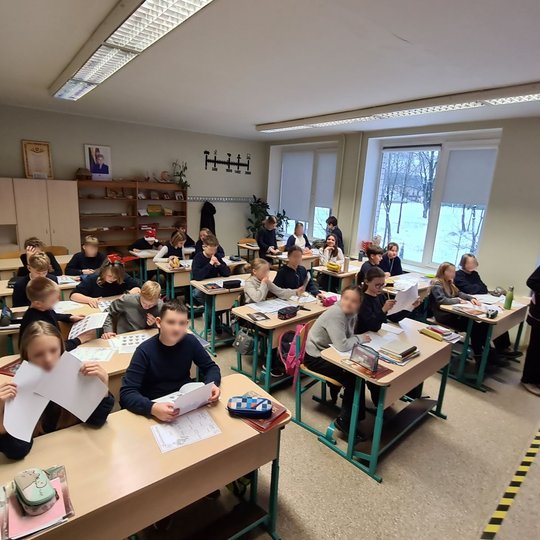 Vaikai klasėje aktyviai varto sąsiuvinius ir baltus lapus.