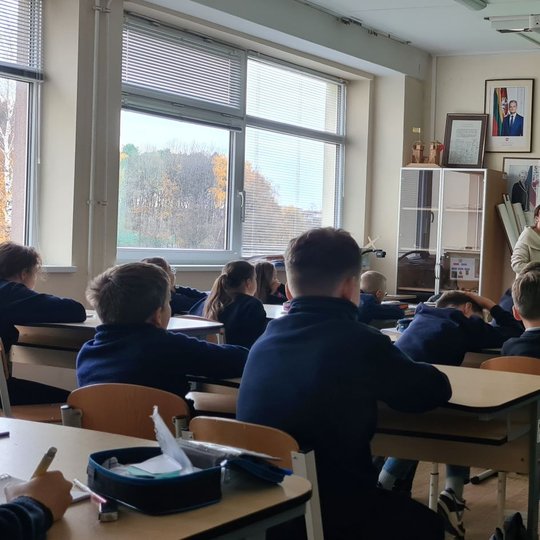 Penktokai žiūri į projektoriaus ekraną ir edukatorę.