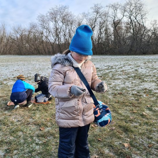 Mergaitė ant Stalo kalno mokosi naudotis skiltuvu. Už jos pora berniukų bando kurti laužą.