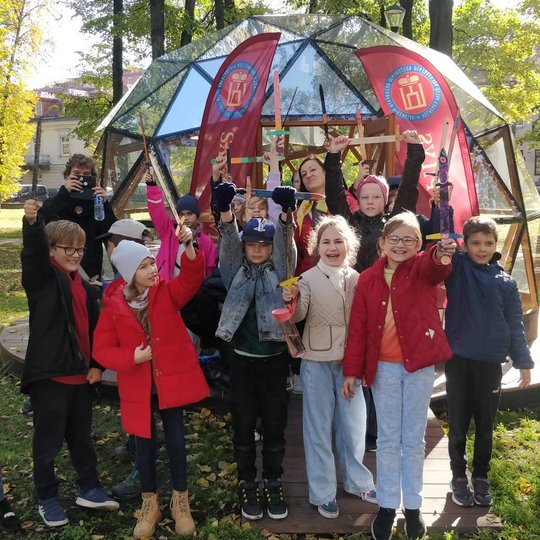 Trečiokai pozuoja nuotraukai su iškeltais mediniai kalavijais, priešais Vilniaus pilių kupolą.