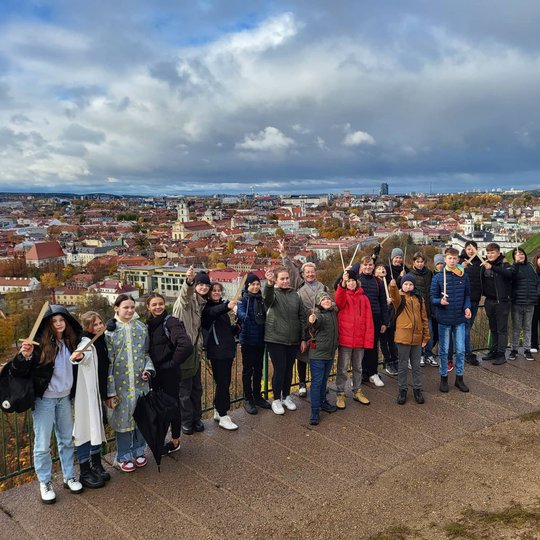 Pavilnio septintokai pozuoja nuotraukai priešais Trijų Kryžių paminklą. Už nugaros matosi Vilniaus senamiesčio panorama. 
