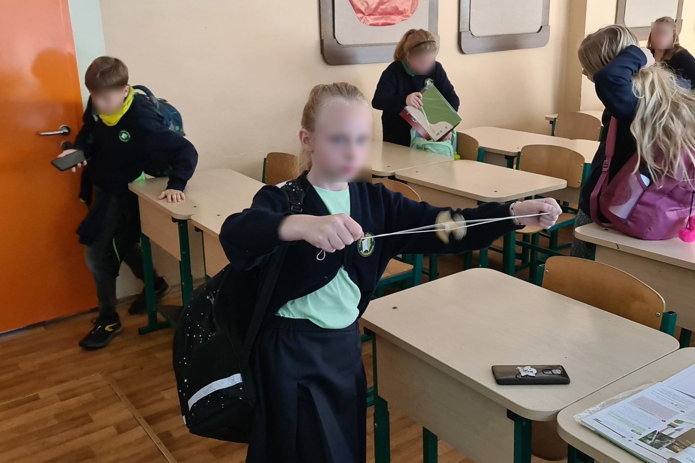 Berniukas žaidžia su siūlu ir verpstuku. Aplink jį laksto kiti mokiniai.