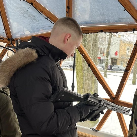 Lankytojas laiko rankose šautuvą. Šalia jo stovi šaulys.