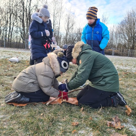 Pora vaikų pritūpę bando kurti laužą. Už jų stovi dar du vaikai.