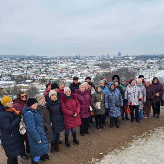 Ekskursijos dalyviai pozuoja nuotraukai priešais Trijų Kryžių paminklą. Jiems už nugarų apsnigta Vilniaus panorama. 
