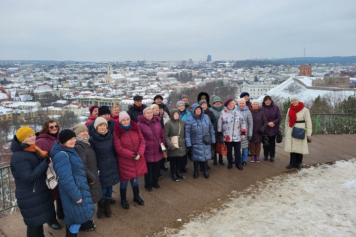 Ekskursijos dalyviai pozuoja nuotraukai priešais Trijų Kryžių paminklą. Jiems už nugarų apsnigta Vilniaus panorama.