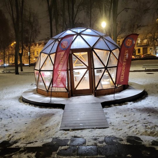Tamsų žiemos vakarą matomas stiklinis kupolas stovi mažame Vilniaus centro parkelyje netoliese nuo gyvenamųjų namų.
