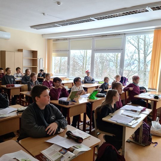 Vaikai klasėje žiūri į projektorių. Visi susikaupę ir įtempę ausis.
