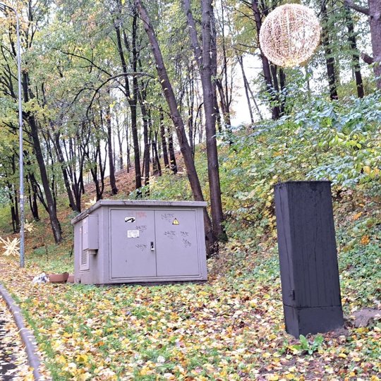 Nuotraukoje elektros transofrmatorinė ir skydinė, kuri ką tik perdažyta juodais dažais. Įrenginiai stovi prie kelio į Trijų kryžių kalną.