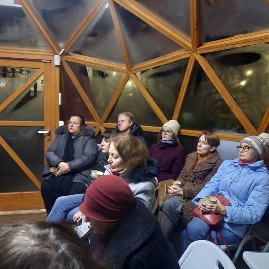 Lauke tamsu, kupolo viduje susėdę edukacijos dalyviai klausosi pasakojimo.