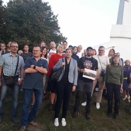 Įvairaus amžiaus žmonių grupė yra ekskursijoje. Visi sustoję ant Trijų kryžių kalno įamžinti akimirką. Nuotraukos fone, dešinėje, matosi trijų kryžių paminklas.