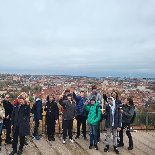 Mokiniai pozuoja nuotraukai ant Trijų Kryžių kalno. Tolumoje matosi Vilniaus panorama.