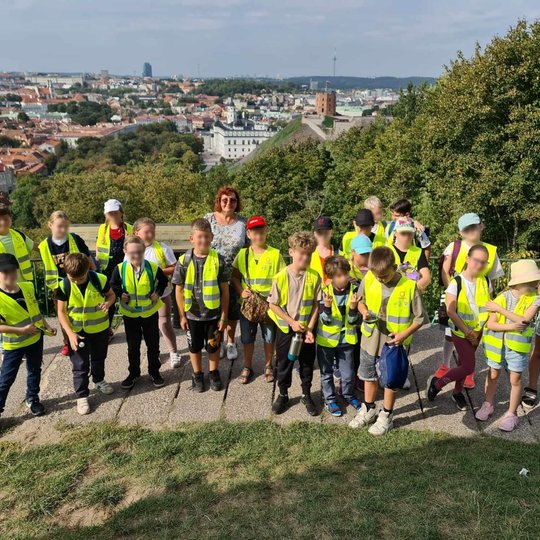 Visi mokiniai, sustoję priešais Vilniaus senamiesčio panoramą, ant Trijų kryžių kalno aikštelės.