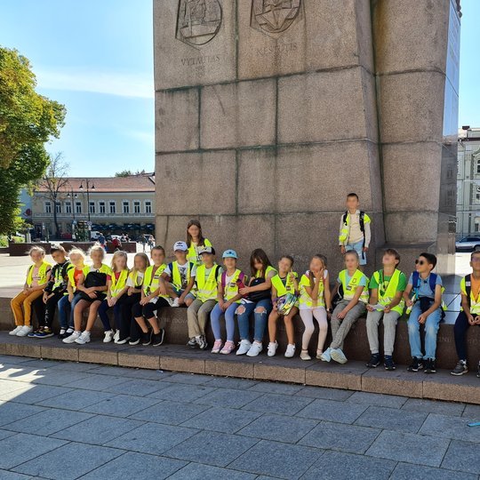 Mokiniai pozuoja susėdę prie kunigaikščio Gedimino paminklo.