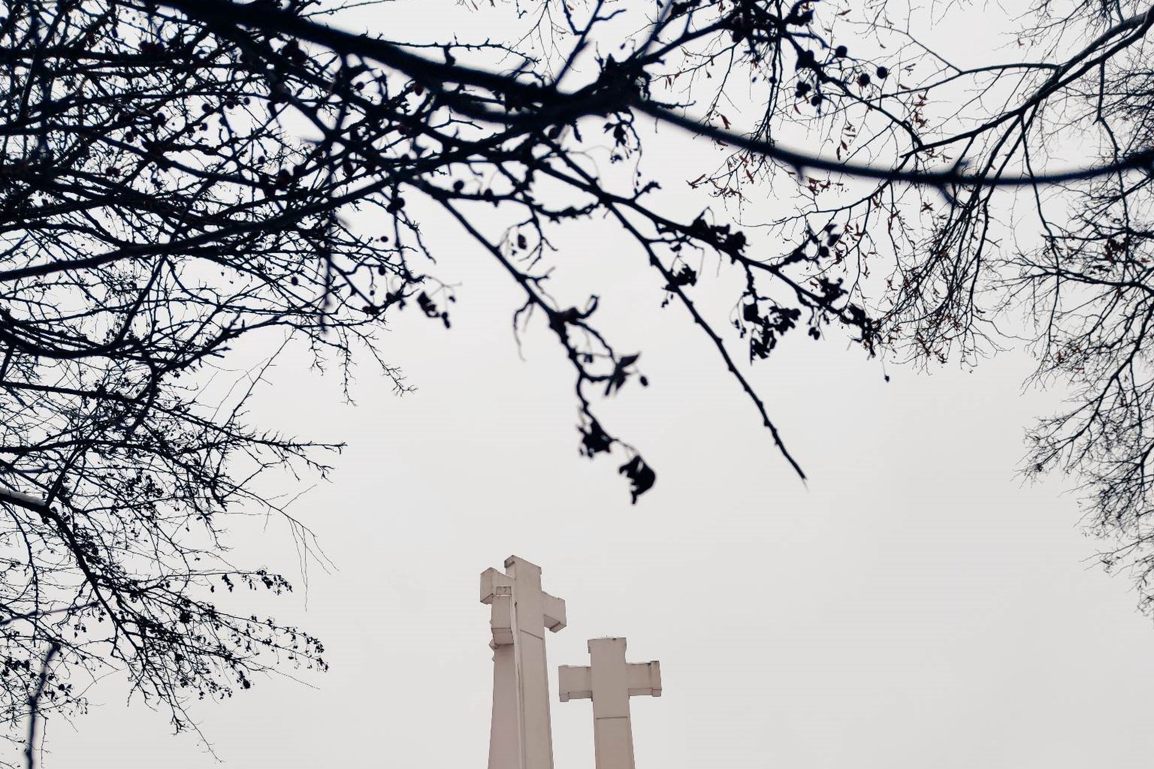 Trijų Kryžių paminklas iš apačios. Priešais keturių praeinančių žmonių siluetai. 