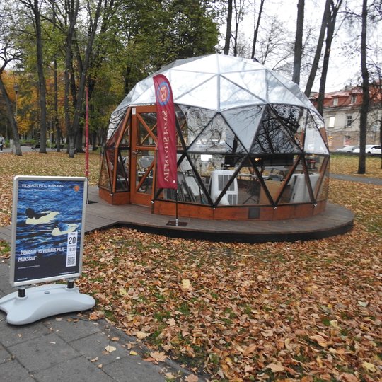 Vilniaus pilių kupolas iš lauko. Šalia vėliavos su Vilniaus pilių rezervato logotipu ir stendas su paskaitos afiša.