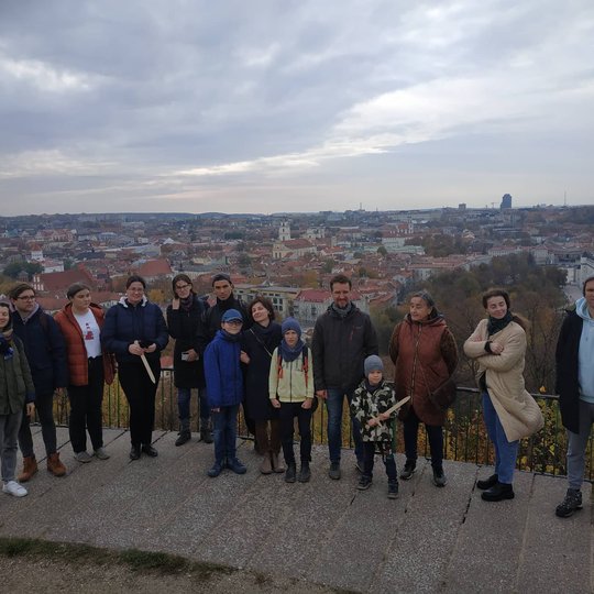 Ekskursijos dalyviai pozuoja nuotraukai ant Trijų Kryžių kalvos. Ekskursantams už nugarų Vilniaus miesto panorama.