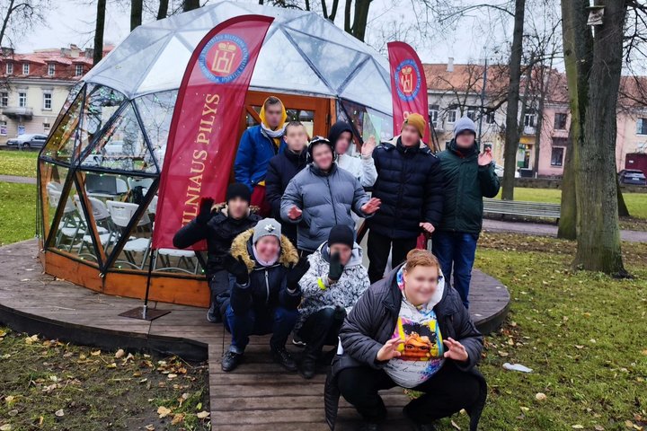 Vilniaus Vilties mokyklos auklėtiniai mojuoja ir pozuoja prie Vilniaus pilių kupolo. Visi nusiteikę žaismingai.