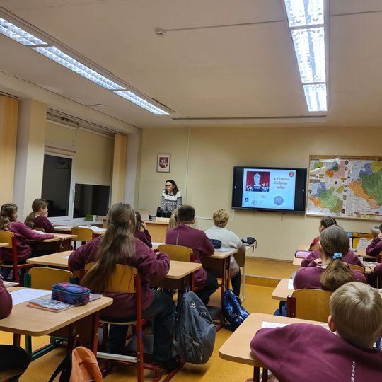 Klasėje, pilnoje mokinių, edukatorė veda istorijos pamoką.